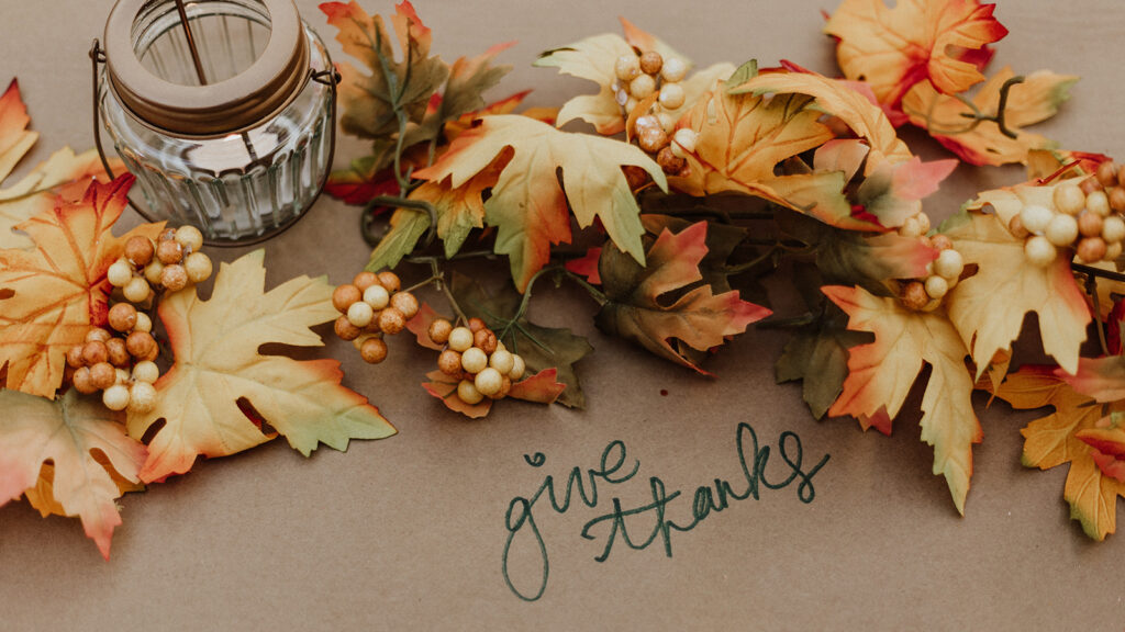 Thanksgiving image of fall leaves and a candle with the text 'give thanks.'